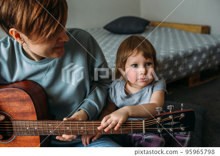 Little girl plays the guitar with her mother on the floor at home Little girl plays the guitar with her mother on the floor at home 95965798