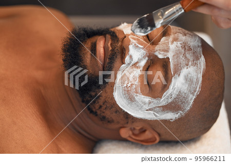 Facial, skincare and relax with black man in spa for beauty, luxury and mud mask. Wellness, therapy and health with male and beautician brush cosmetics product on face for peace, massage and salon 95966211