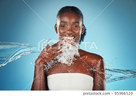 Black woman, water and splash with beauty portrait of happy skincare, shower and wellness. Hydration, fresh and clean hygiene with face model for luxury, relax and spa in a blue background in studio 95966520