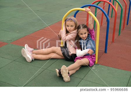 A child with a cast on his arm is playing with a friend on the playground in the yard. Life and health insurance 95966686