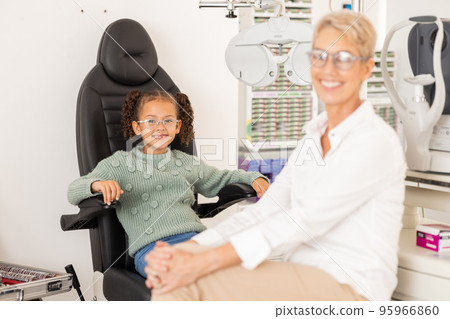 Children, vision and glasses with a girl customer and optometrist consulting in an office for an eye test. Portrait, eyewear and retail with a female child and optician consulting in an appointment 95966860
