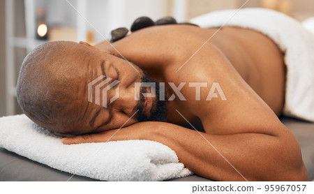 Black man, spa bed hot stone massage and relax body, treatment and luxury physical therapy for health, calm and wellness. Zen man, rest salon and rock for healthcare, recovery or skincare on back Black man, spa bed hot stone massage and relax body, treatment and luxury physical therapy for health, calm and wellness. Zen man, rest salon and rock for healthcare, recovery or skincare on back 95967057