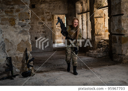 Blonde woman in army uniform holding a firearm in an abandoned building. Blonde woman in army uniform holding a firearm in an abandoned building. 95967703