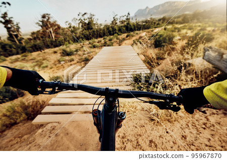 POV perspective, mountain bike and man cycling on hill, bridge and path for adventure, speed and sports challenge, action and off road race in nature. Bicycle handle, athlete and outdoor competition POV perspective, mountain bike and man cycling on hill, bridge and path for adventure, speed and sports challenge, action and off road race in nature. Bicycle handle, athlete and outdoor competition 95967870