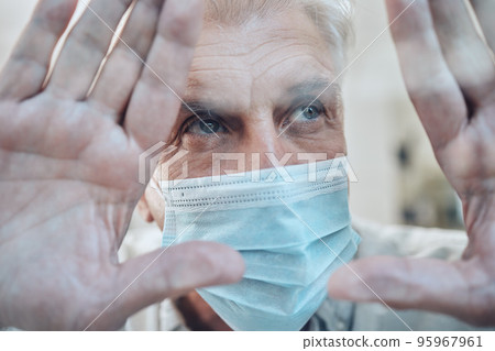 Hands, covid and quarantine with a senior man in a mask standing behind glass in a house during lockdown. Window, sad and isolated with a mature male in a retirement home during corona virus pandemic 95967961