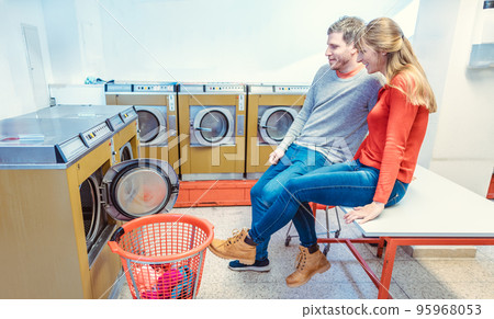Couple in laundromat watching the laundry Couple in laundromat watching the laundry 95968053