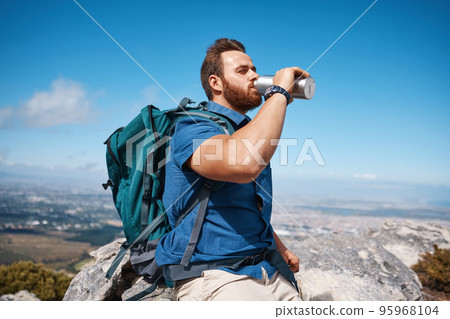 Hiking, fitness and view with a man drinking water while taking a break from walking in nature for exercise. Mountain, health and summer with a male hiker having a drink from a bottle while exploring 95968104