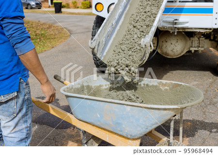 Mixer truck pours concrete into wheelbarrow at construction site Mixer truck pours concrete into wheelbarrow at construction site 95968494