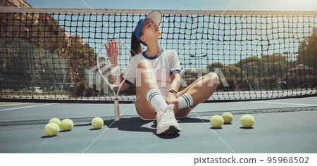 Tennis, athlete and woman ready for a tennis match while sitting on the court with tennis balls. Fitness, active and young girl holding a tennis racket and ball ready for training or playing game Tennis, athlete and woman ready for a tennis match while sitting on the court with tennis balls. Fitness, active and young girl holding a tennis racket and ball ready for training or playing game 95968502