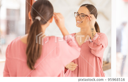 Woman, glasses and mirror at optometrist, new frame and lense for vision, eye and eyesight after shopping in store. Customer choosing, buying and decide for frames for better vision and healthcare Woman, glasses and mirror at optometrist, new frame and lense for vision, eye and eyesight after shopping in store. Customer choosing, buying and decide for frames for better vision and healthcare 95968516