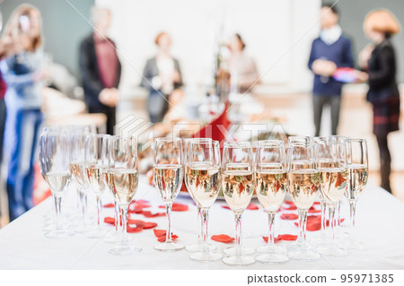 Banquet event. Table with the wineglasses, snacks and cocktails. People celebrating in the background Banquet event. Table with the wineglasses, snacks and cocktails. People celebrating in the background 95971385