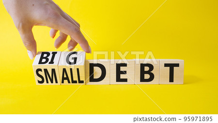 Big debt and small debt symbol. Businessman hand. Turned cubes with words Big debt and small debt. Beautiful yellow background. Business concept. Copy space 95971895