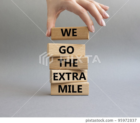 We go the extra mile symbol. Wooden blocks with words 'We go the extra mile'. Beautiful grey background. Businessman hand. Business and 'We go the extra mile' concept. Copy space. We go the extra mile symbol. Wooden blocks with words 'We go the extra mile'. Beautiful grey background. Businessman hand. Business and 'We go the extra mile' concept. Copy space. 95972837