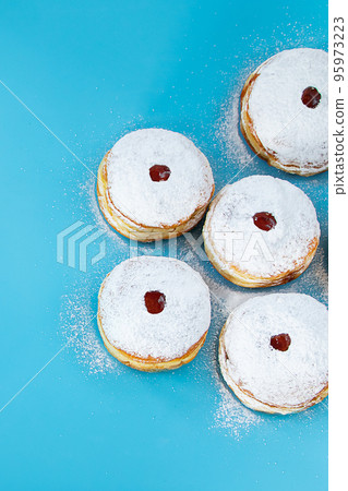 Symbols of Jewish religious holiday Hanukkah. Traditional dessert donuts sufganiyot on blue background. 95973223
