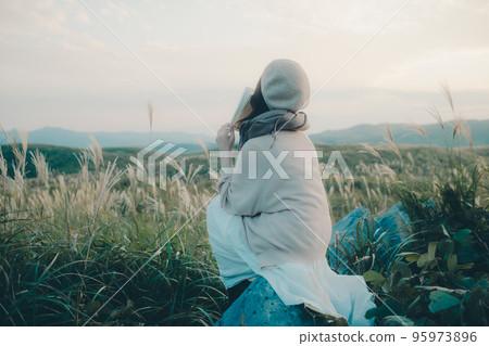 Photo of a woman reading in nature at sunset 95973896