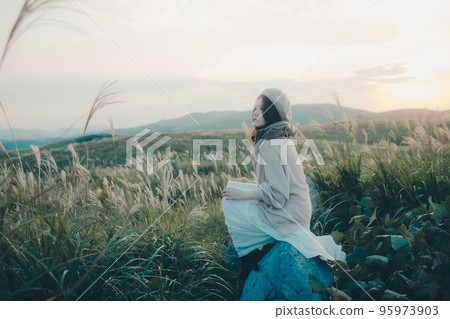 Photo of a woman reading in nature at sunset 95973903