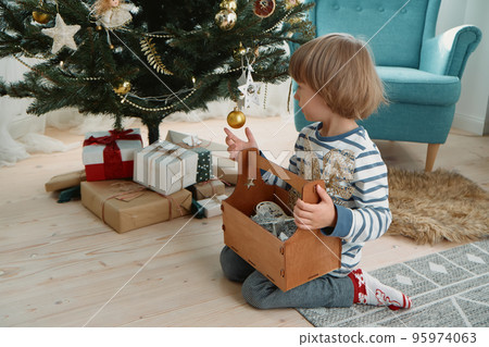 Child decorating a Christmas tree sitting in pajamas in a home interior Child decorating a Christmas tree sitting in pajamas in a home interior 95974063