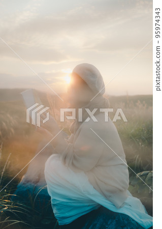 Photo of a woman reading in nature at sunset 95974343