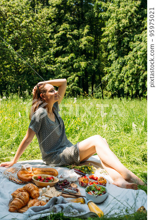 Beautiful woman on picnic. She smiles, eats strawberries and enjoys summer. 95975021