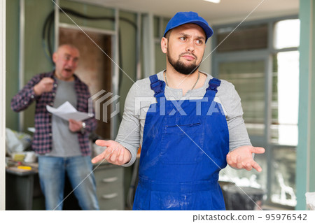 Perplexed builder in building under renovation with screaming customer Perplexed builder in building under renovation with screaming customer 95976542