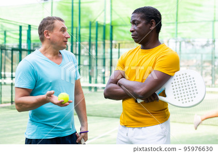 Men chatting on outdoor padel tennis court 95976630