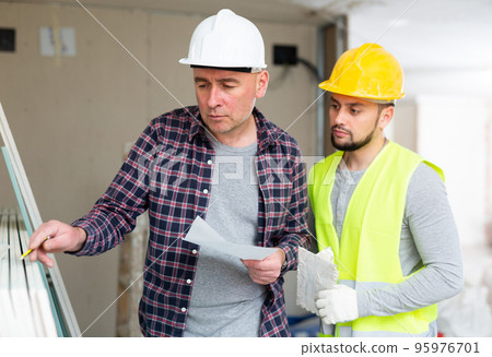 Adult designer with papers talking to contractor in building during renovation 95976701
