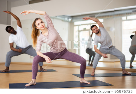 Woman performing stretching during group yoga training Woman performing stretching during group yoga training 95976725