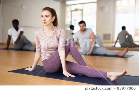 Woman with group doing stretching workout in yoga studio Woman with group doing stretching workout in yoga studio 95977006