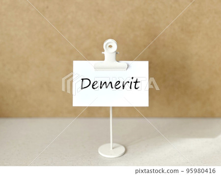 Clip stand and white paper with Demerit letters_cork background 95980416