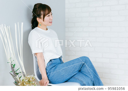 穿著牛仔褲的日本女人，雙腿交叉在房間的椅子上 95981056