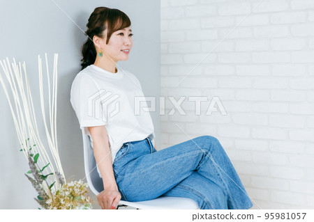 Japanese woman in denim with her legs crossed on a chair in the room Japanese woman in denim with her legs crossed on a chair in the room 95981057