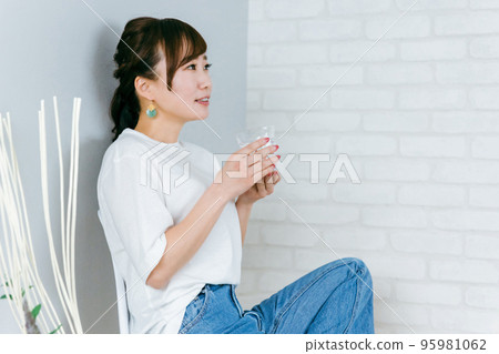 Asian woman in jeans drinking water from a water server while sitting on a chair in the room 95981062