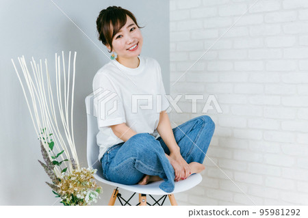 穿著牛仔褲的時尚日本女人盤腿坐在椅子上 95981292