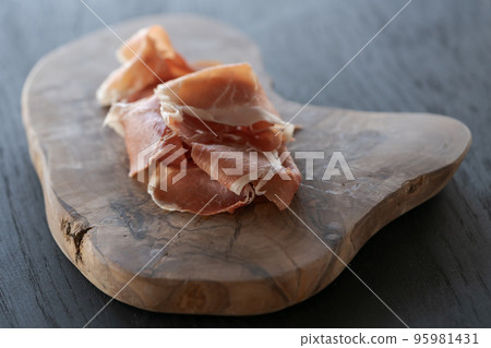 Thin slices of jamon on olive wood board Thin slices of jamon on olive wood board 95981431