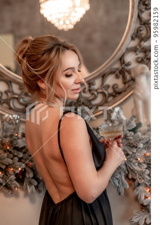 Portrait of a wealthy mature woman with evening makeup and hairstyle posing in a black dress against the backdrop of a Christmas room. Luxurious lifestyle. Cosmetology, plastic surgery, rejuvenation. 95982159