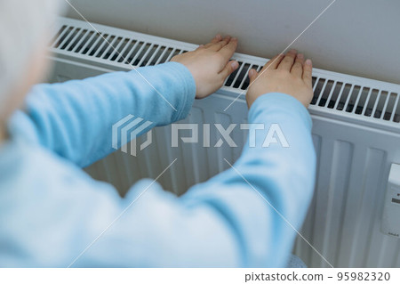 child warming hands over heater. Energy crisis in Europe 95982320