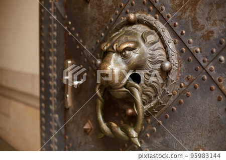 A door knocker in the shape of a lion adorns an old door 95983144