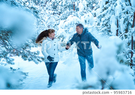 A young couple in love fooling around in the winter woods playing and throwing snow at each other A young couple in love fooling around in the winter woods playing and throwing snow at each other 95983716