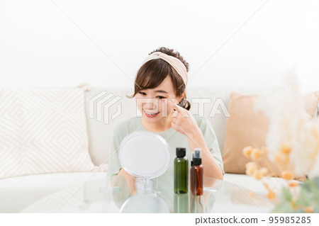 A woman looking in the mirror with a smile at home (eyes / contact lenses) 95985285