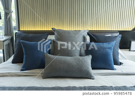 Blue pillow on king size bed in contemporary bedroom with modern lamp and vase on nightstand table. 95985478