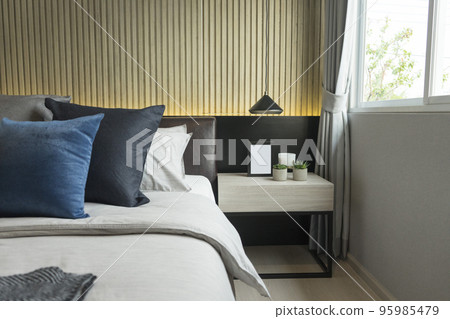 Blue pillow on king size bed in contemporary bedroom with modern lamp and vase on nightstand table. 95985479
