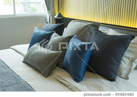 Blue pillow on king size bed in contemporary bedroom with modern lamp and vase on nightstand table. 95985480