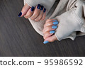 Gel nail design.Beautiful manicure. Nail polish is applied to the hand, polish is a blue color. Blue background closeup. Multi-colored blue manicure. 95986592