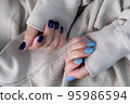 Gel nail design.Beautiful manicure. Nail polish is applied to the hand, polish is a blue color. Blue background closeup. Multi-colored blue manicure. 95986594