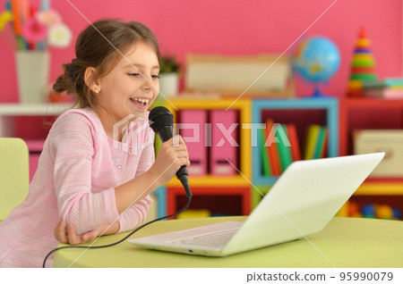 Adorable little girl singing karaoke with modern laptop Adorable little girl singing karaoke with modern laptop 95990079