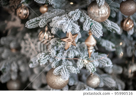Close-up of a festively decorated outdoor Christmas tree with balls on a blurred sparkling fairy background. Defocused garland lights, bokeh effect. 95990516