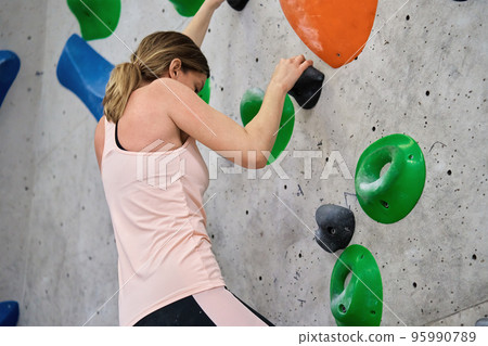 Woman climbing up on wall at bouldering gym. Female climber training, hanging on bouldering climbing wall. Active lifestyle and extreme sport concept. 95990789