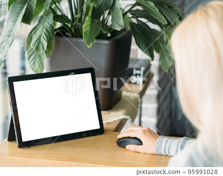 Distance work. Digital mockup. Online connection. Unrecognizable woman sitting desk working tablet computer blank screen using mouse in light room interior. 95991028