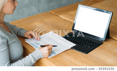 Accountant manager. Computer mockup. Office work. Female worker sitting desk with laptop blank screen checking documents in light room interior. 95991030