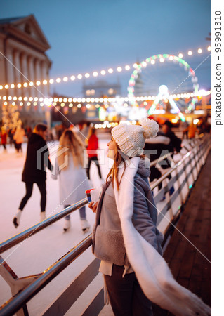 Smiling woman in winter style clothes with coffee near skating rink. Young woman enjoying winter holidays. Smiling woman in winter style clothes with coffee near skating rink. Young woman enjoying winter holidays. 95991310